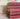 A pile of five red old books stacked on top of each other in front of a floral wallpaper background.